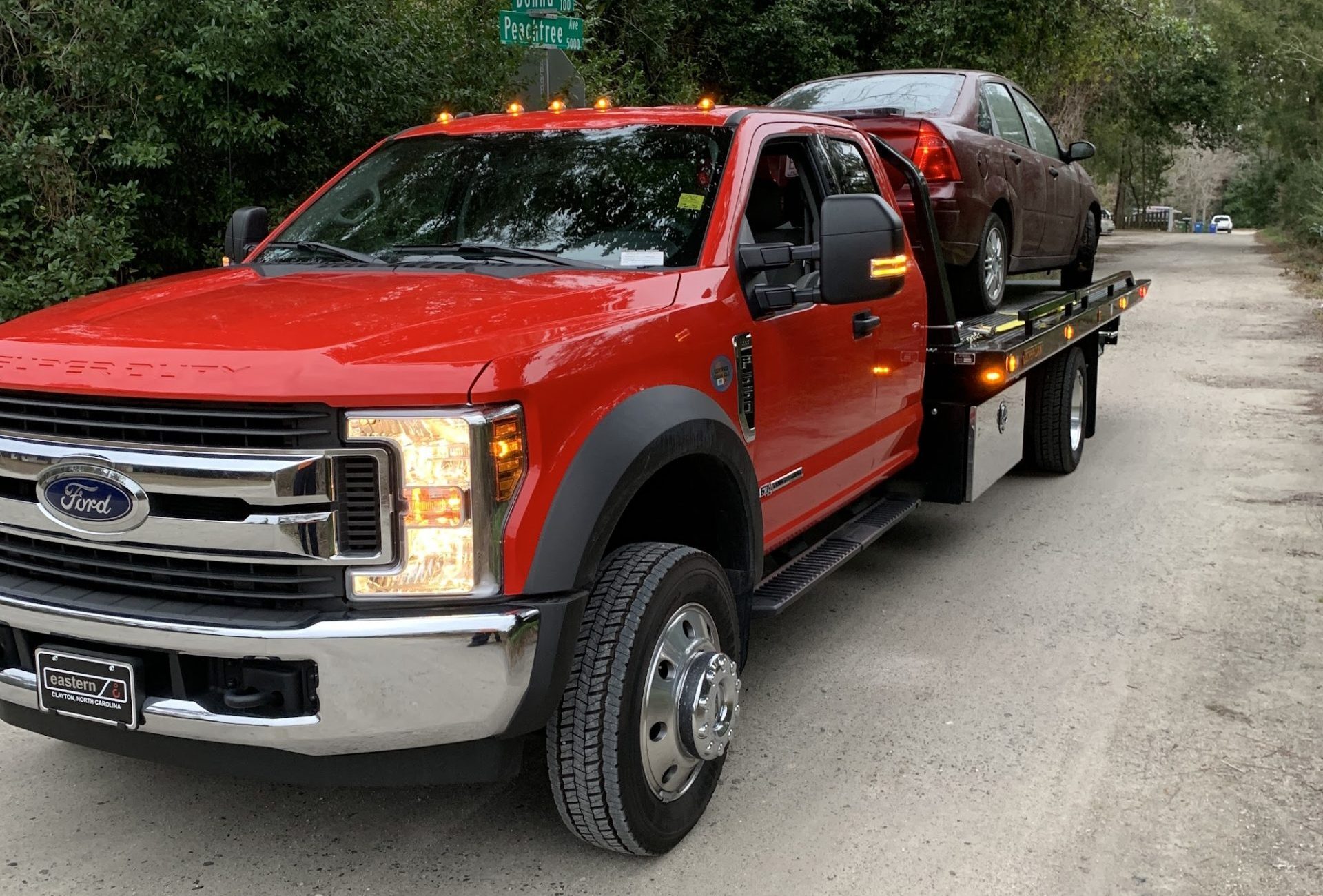 Red flatbed tow truck transporting a car